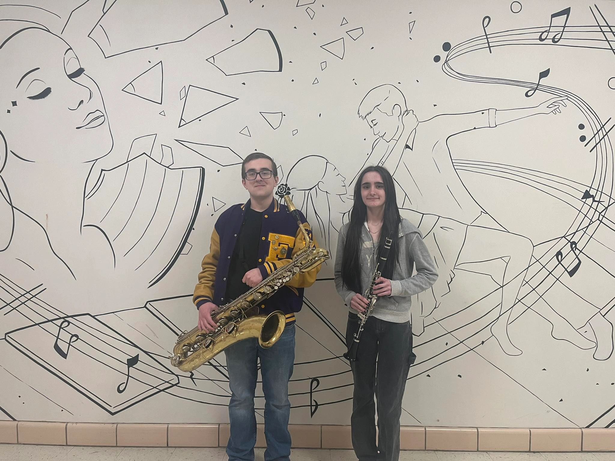 Two people holding musical instruments in front of a wall with musical and artistic drawings, including a woman, a man, and musical notes.