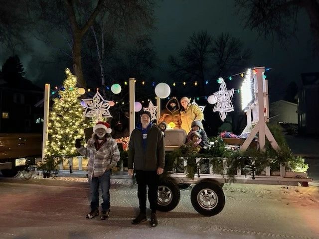 People standing in front of a decorated Christmas display with trees, stars, and lights at night.