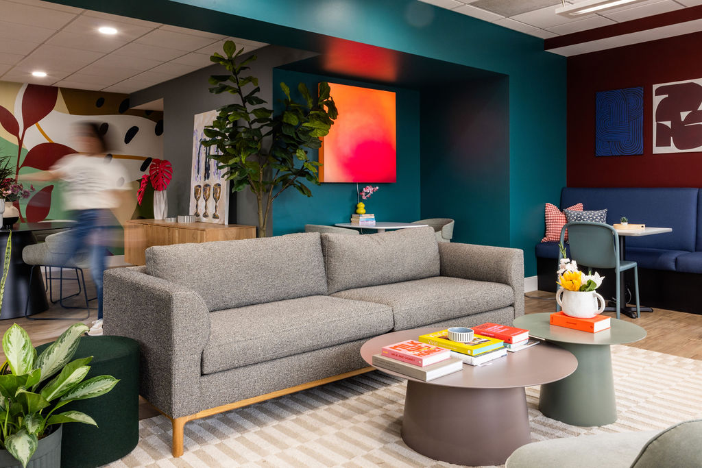 Modern living room with gray sofa, colorful wall art, and a round coffee table with books and a flower arrangement.