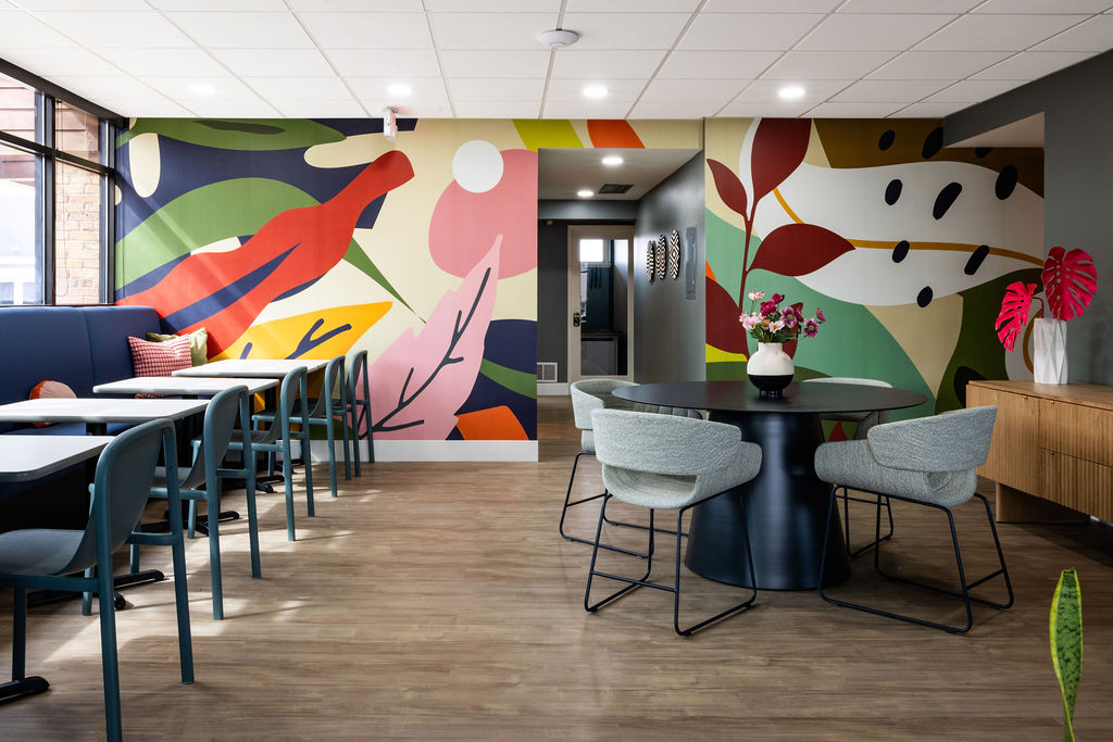 Interior room with colorful abstract wall art, a round table with chairs, and a sideboard with plants.
