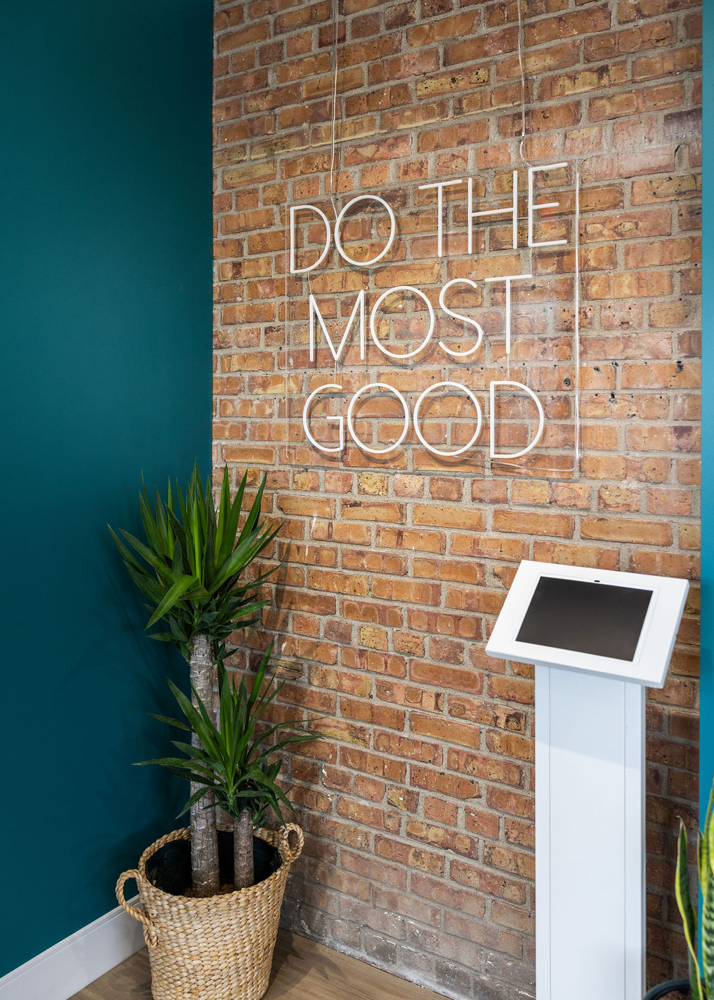 Brick wall with white text reading 'DO THE MOST GOOD' and a potted plant in a woven basket.