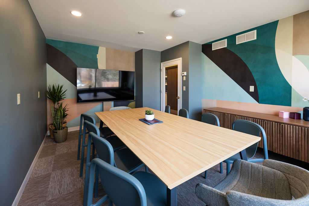 Modern dining room with a wooden table, six chairs, a large window, and a colorful geometric wall design.