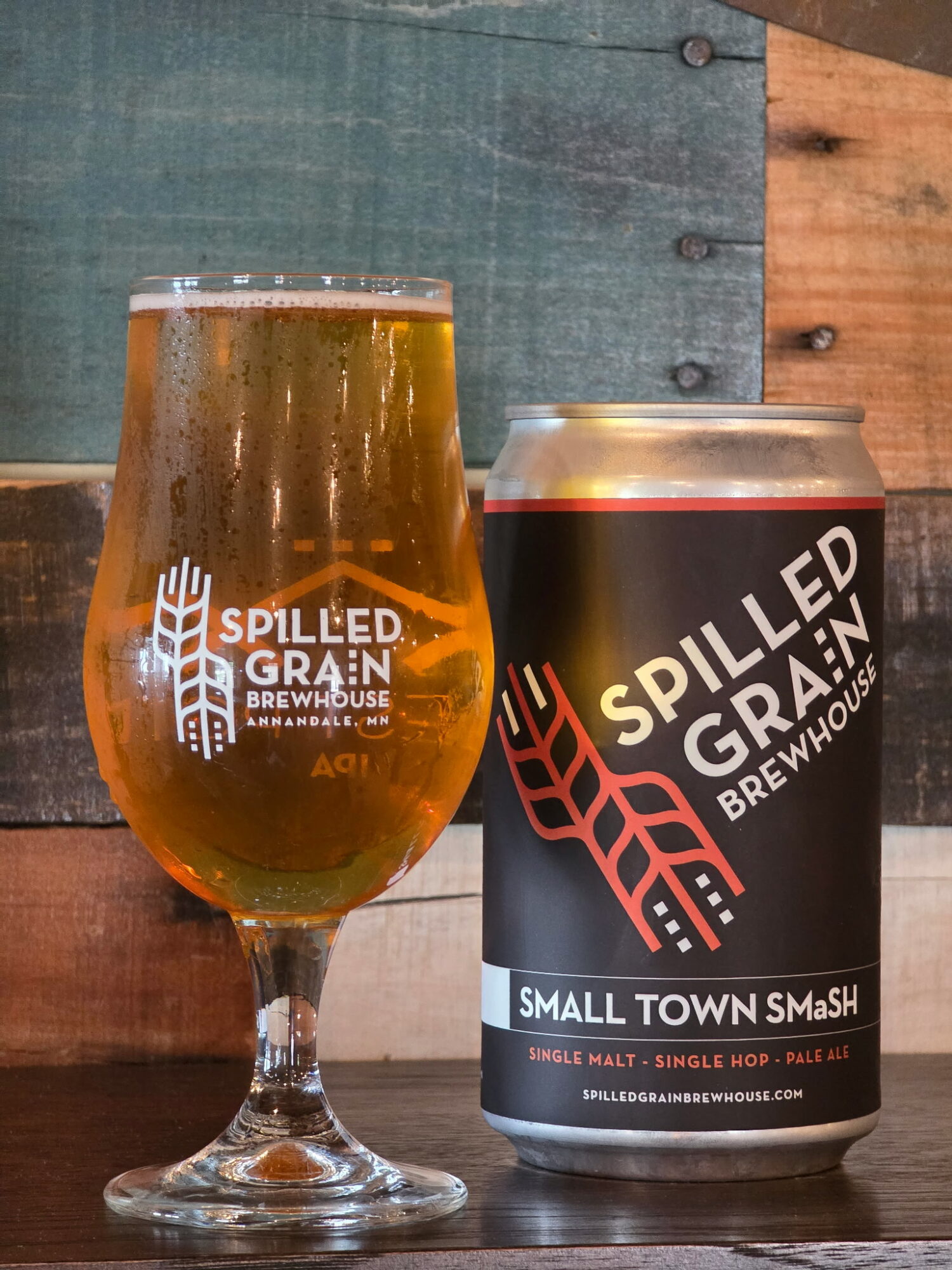 A glass of beer and a can of Spilled Grain Brewhaus beer on a wooden surface, with a wooden and painted background.