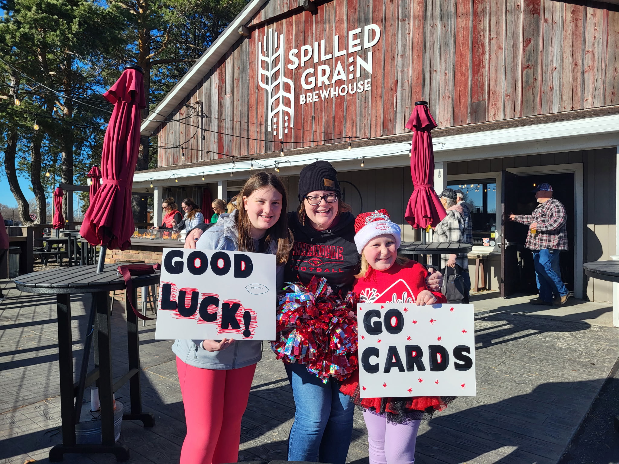 Three people holding signs outside a building with a sign that reads 'Splitted Grain Brewery.'