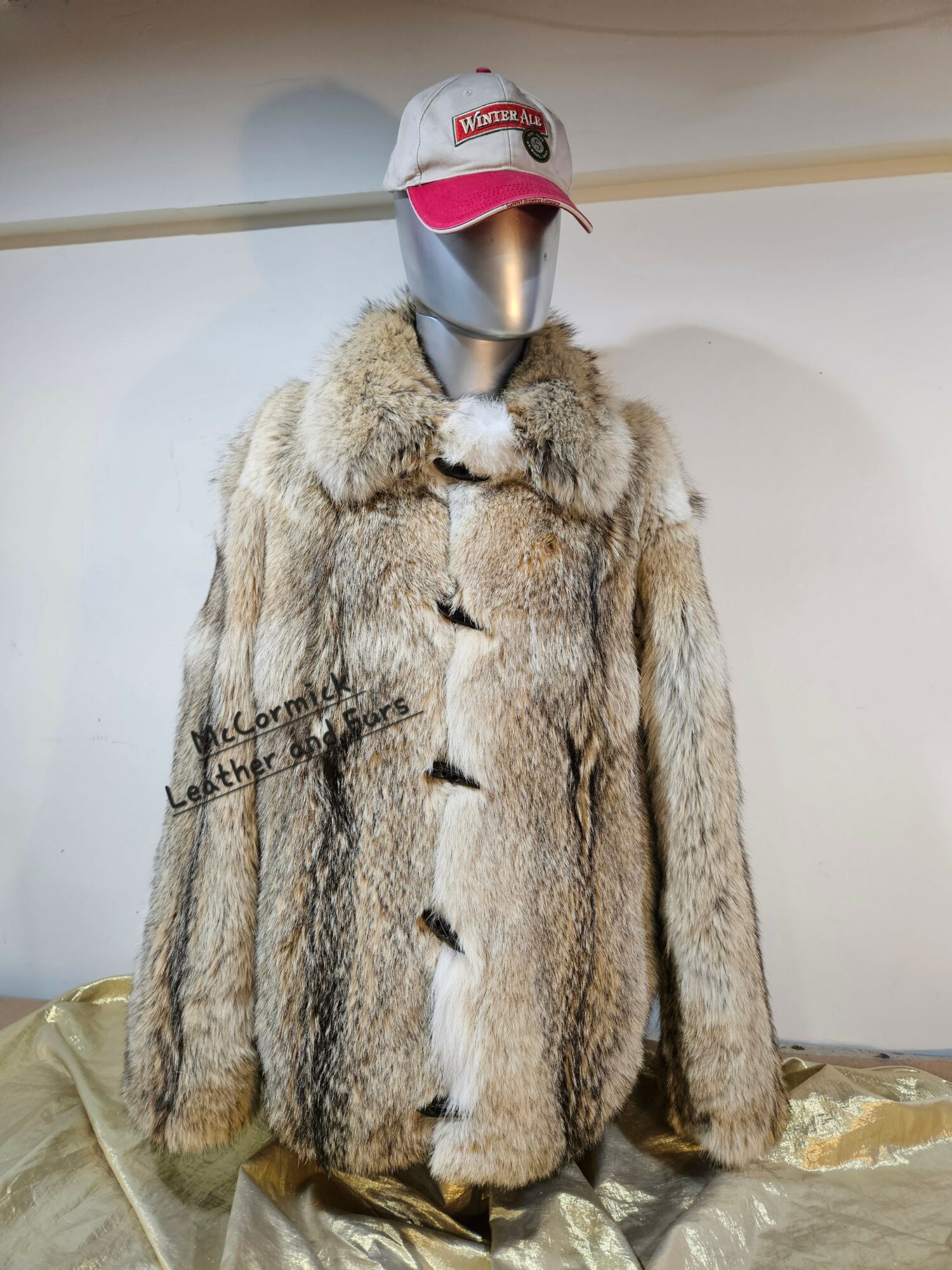 Mannequin wearing a fur coat and a white and pink baseball cap, headless, against a plain background.