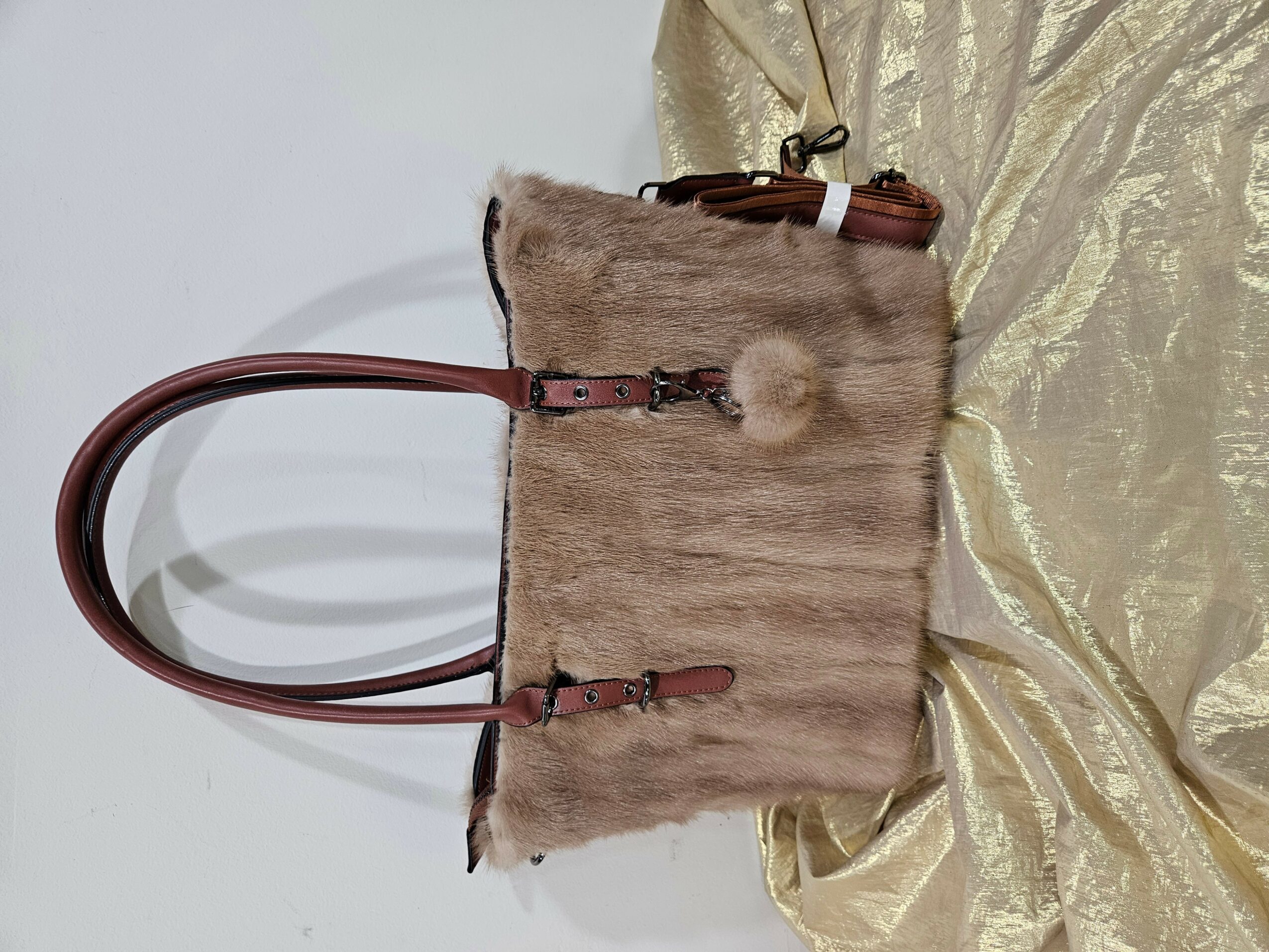Fur handbag with brown handles on gold fabric, viewed from the side.
