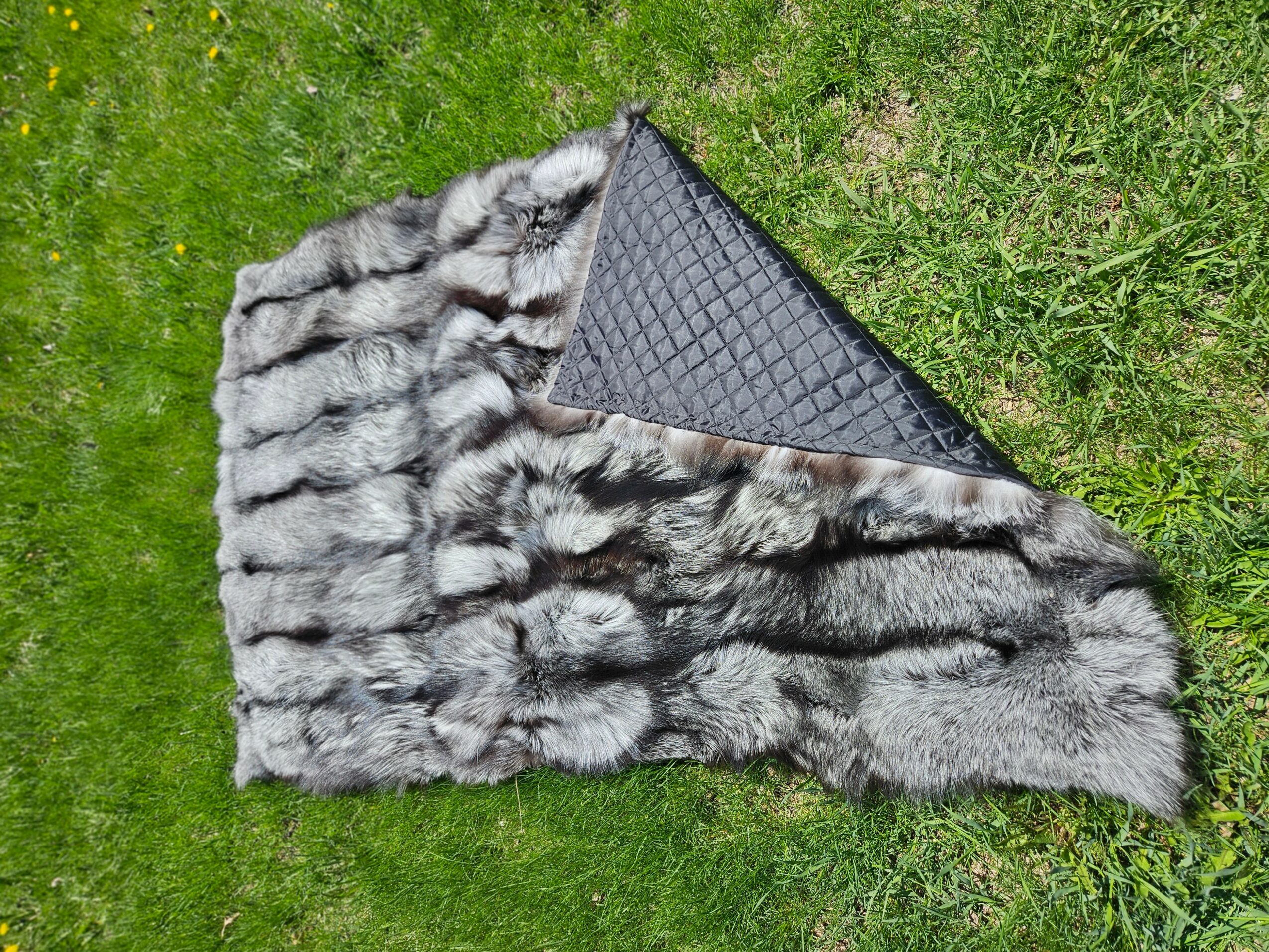 Gray fur blanket draped over a black textured surface on green grass, with a fur pattern visible.