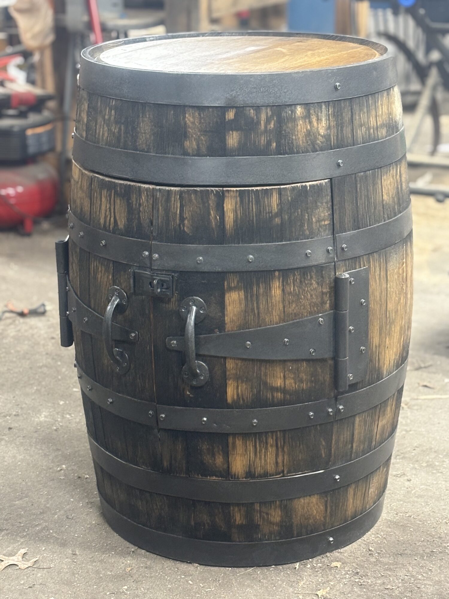 Wooden barrel with metal bands and handles, standing outdoors on a paved surface.