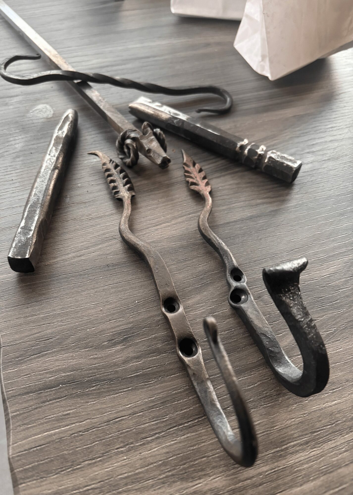 Tools and utensils on a dark wooden surface, including tongs, a hook, and a metal rod.