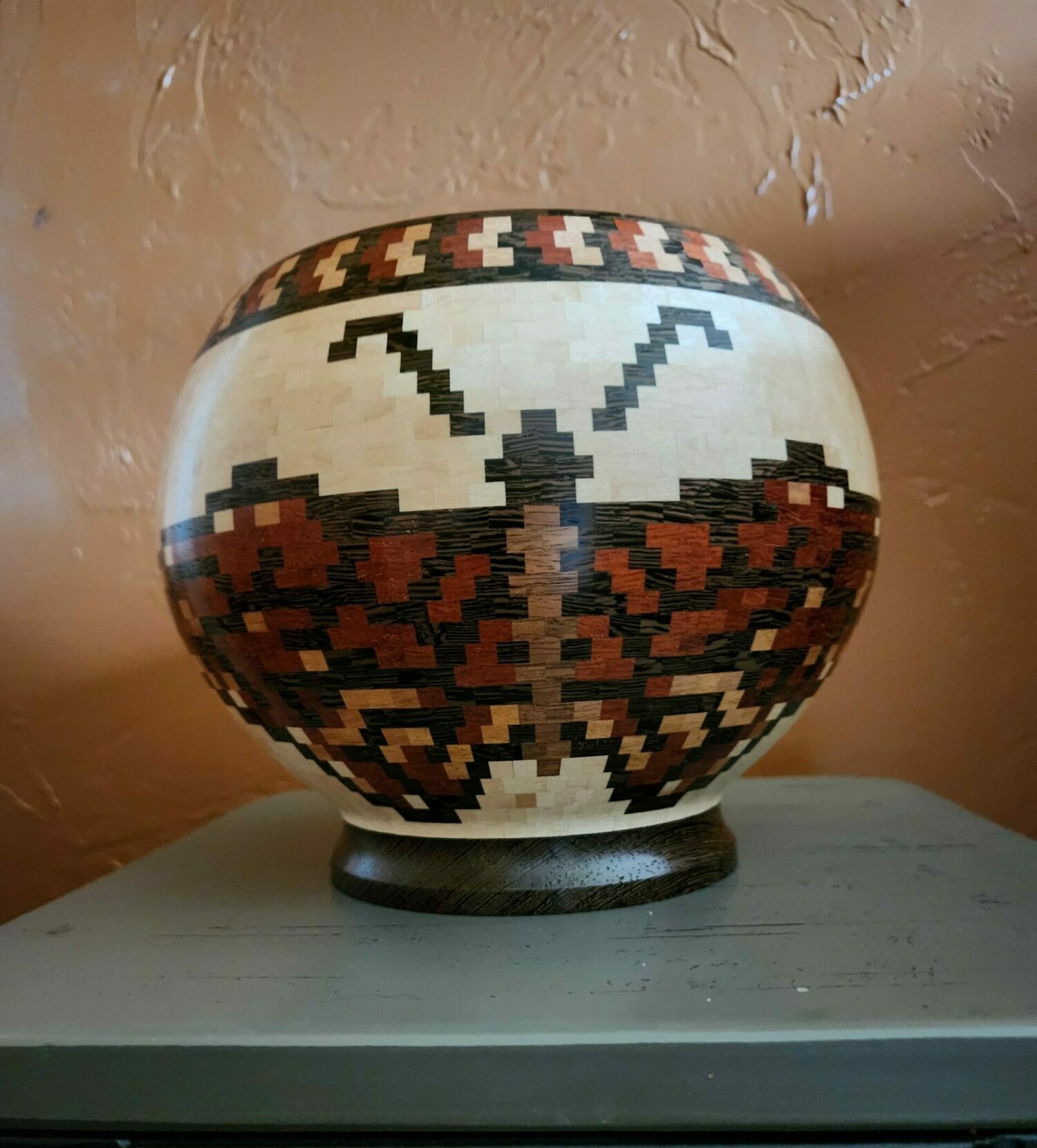 Decorative spherical object with pixelated patterns, placed on a gray surface against a textured orange wall.