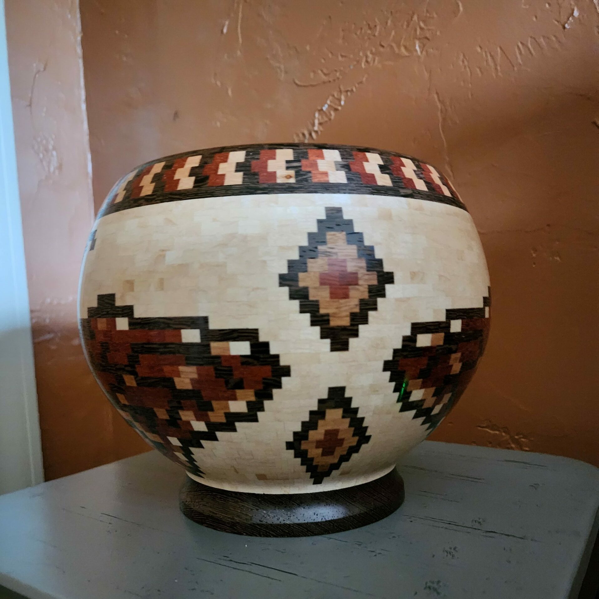 Decorative ceramic pot with geometric patterns on a table against a wall.