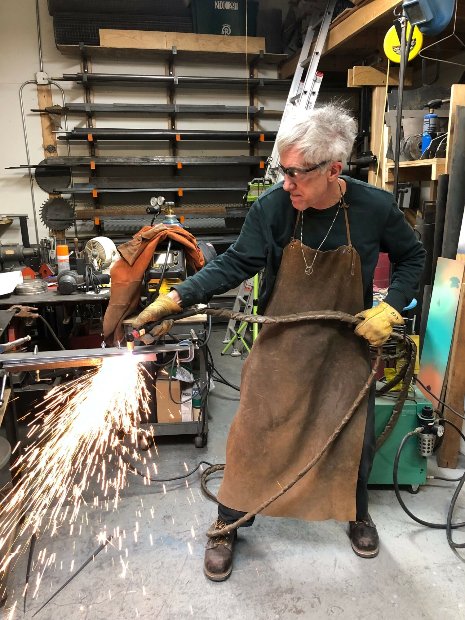 Person welding metal with sparks flying, wearing protective apron and gloves, in workshop setting.