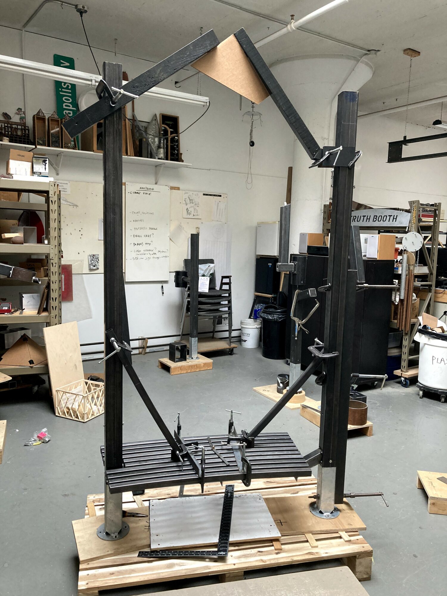 A black mechanical device with arms and a platform, mounted on a wooden pallet in a workshop.