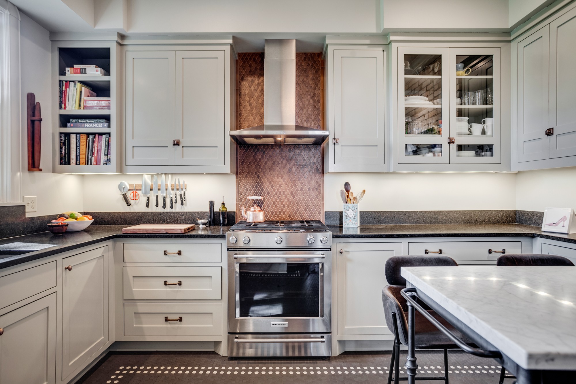 Kitchen with light-colored cabinets, a stove, and a marble countertop, with a table and chairs in the foreground.