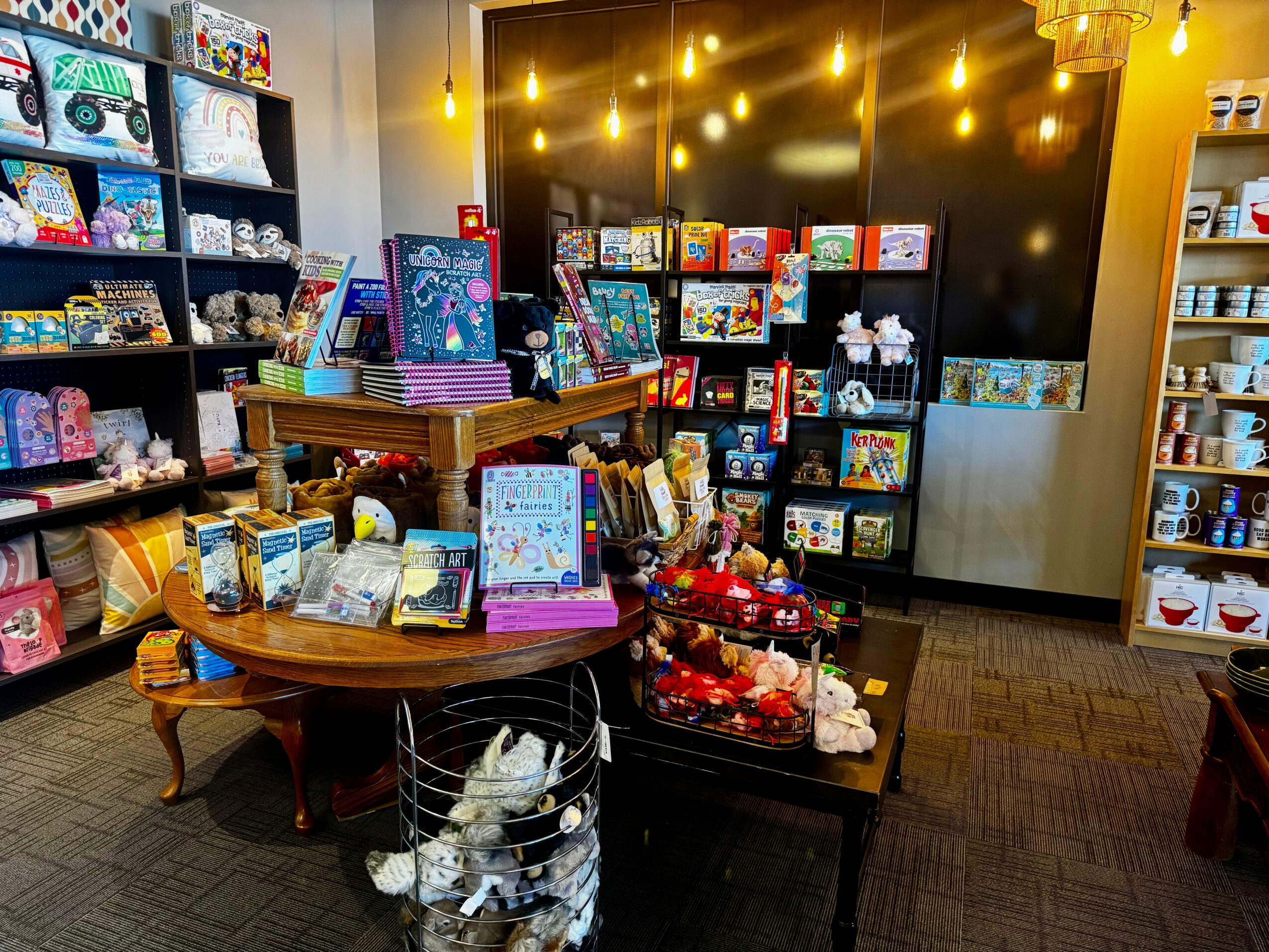 Gift shop with shelves of toys, books, and decorations, warm lighting, and a table with holiday-themed items.
