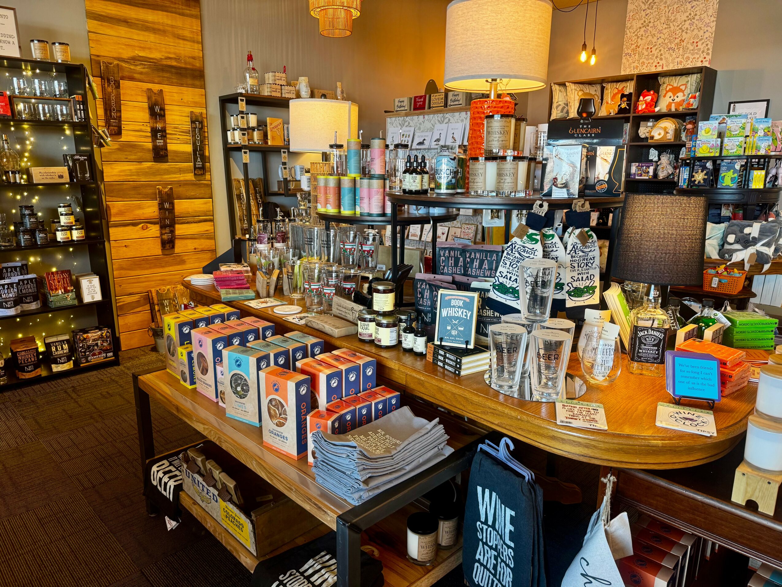 Display of various products on a wooden counter in a store, with shelves and lamps in the background.