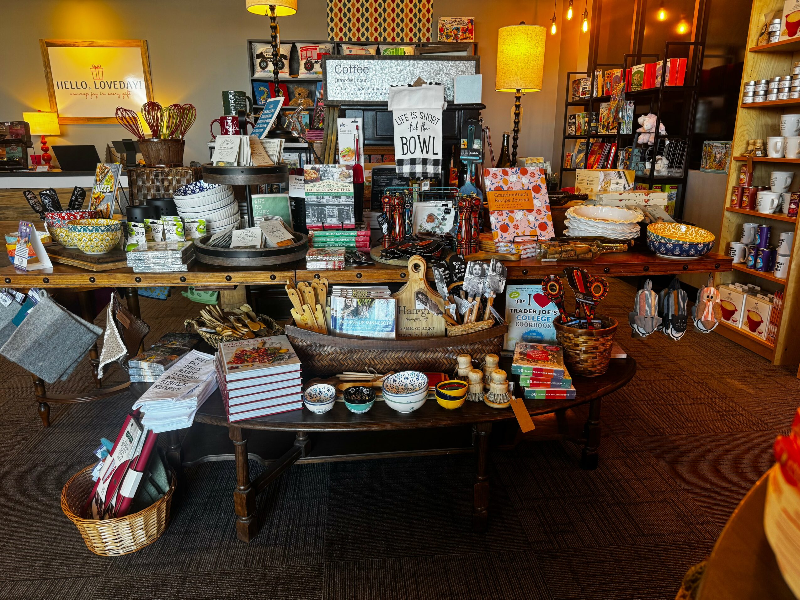 Display of various bowls, plates, and kitchenware on tables and shelves in a store, with warm lighting and colorful items.