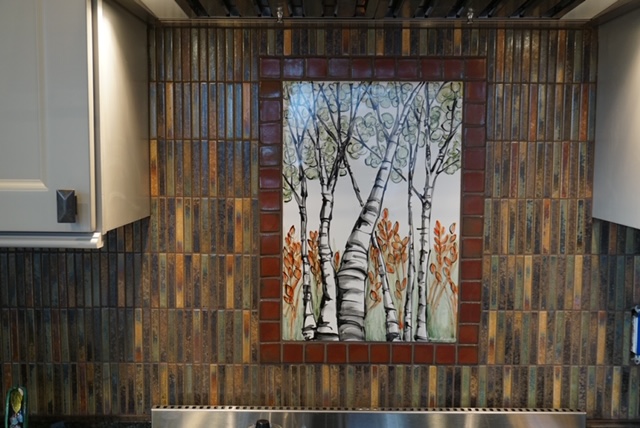 Wall with a framed painting of trees and sky, surrounded by multicolored wooden panels, in a room interior.