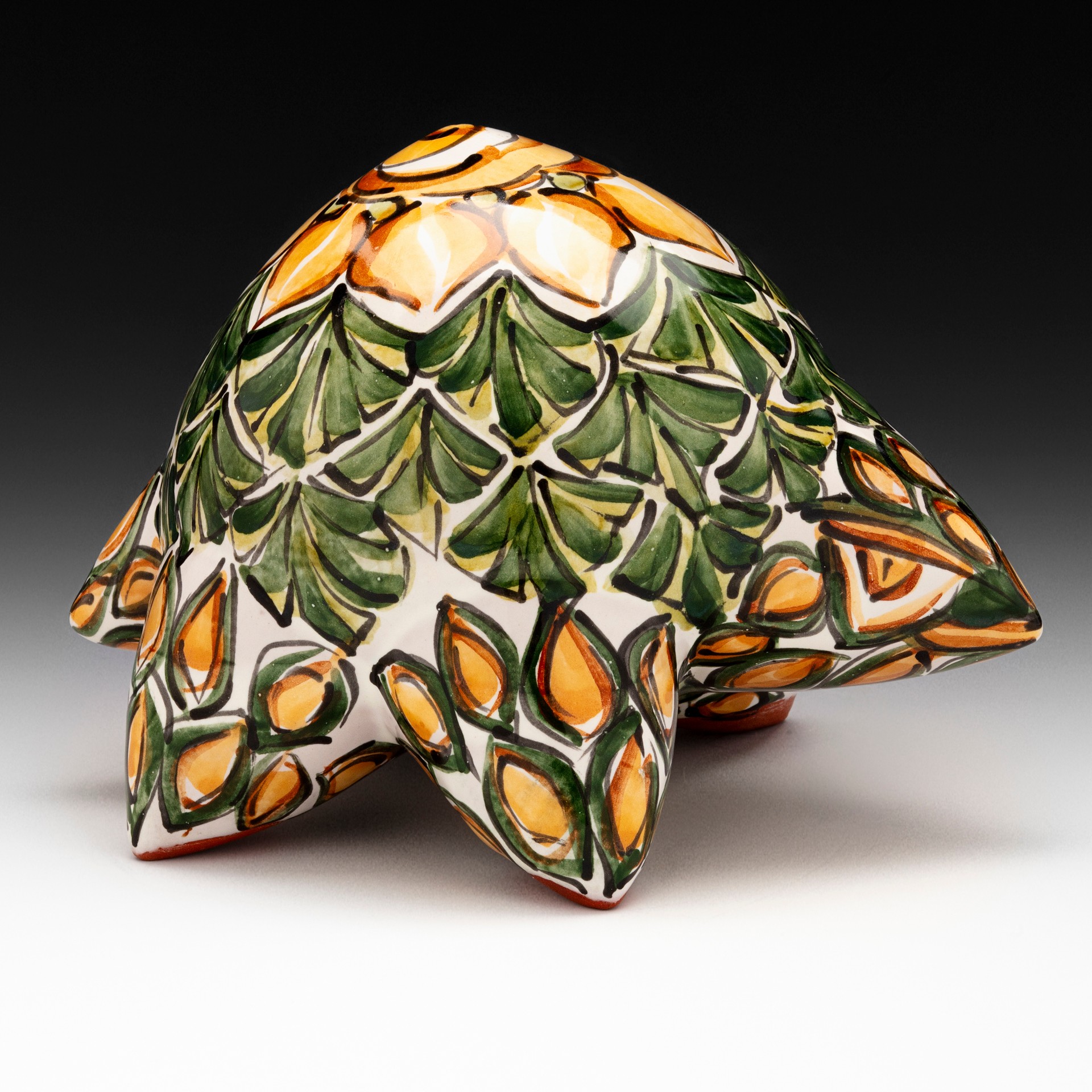 Decorative ceramic sculpture with leaf and flower patterns in green, orange, and cream colors, set against a black background.