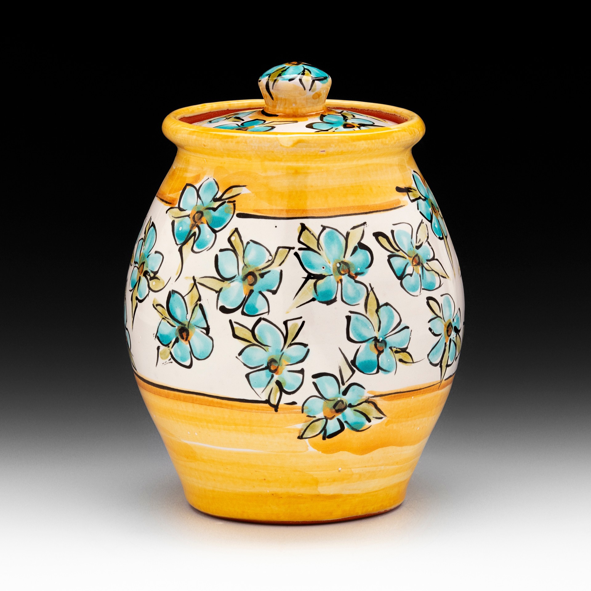 Decorative ceramic jar with a lid, yellow and white stripes, blue flowers, and black outlines, against a black background.