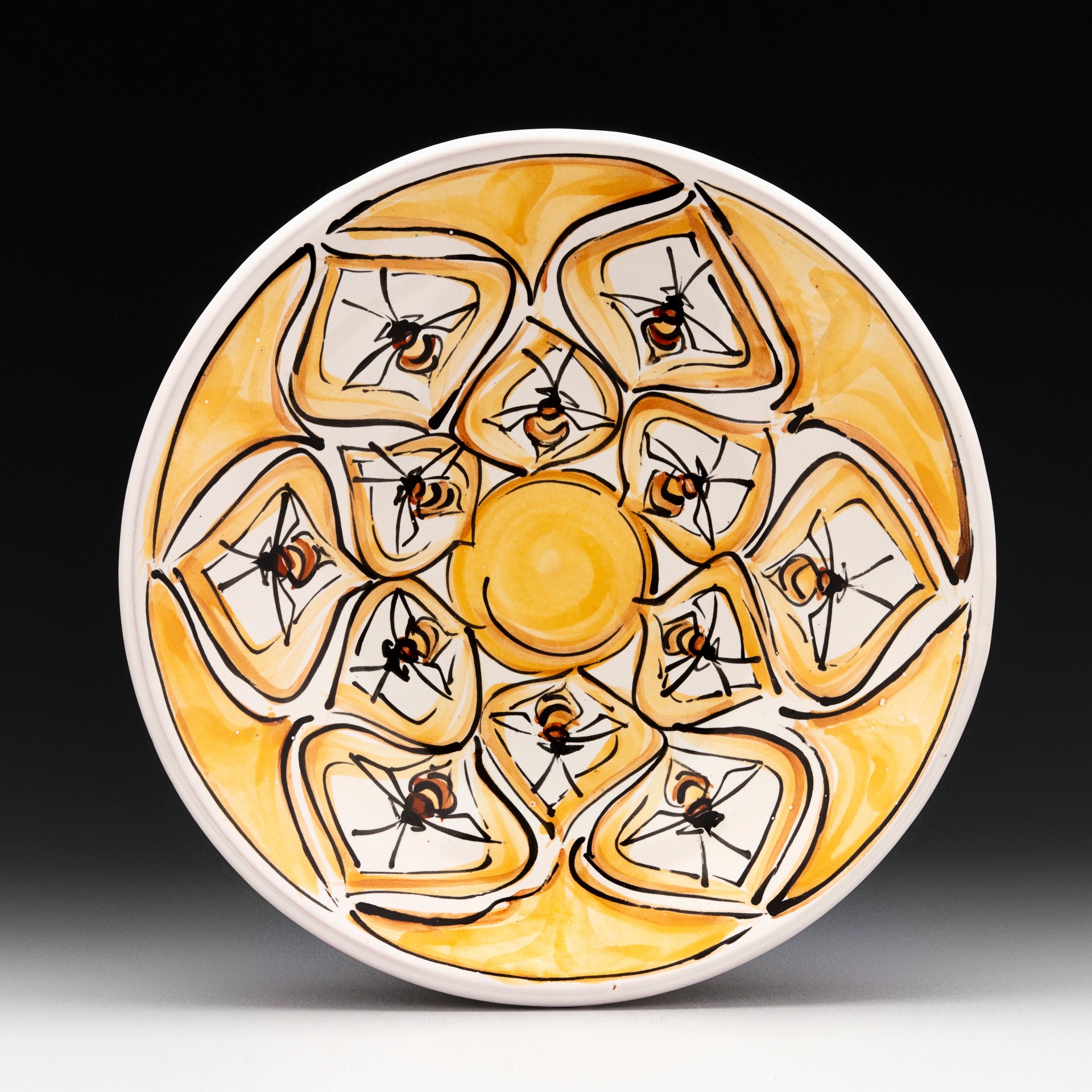 Decorative plate with a yellow and black pattern featuring ants and geometric shapes, on a black background.