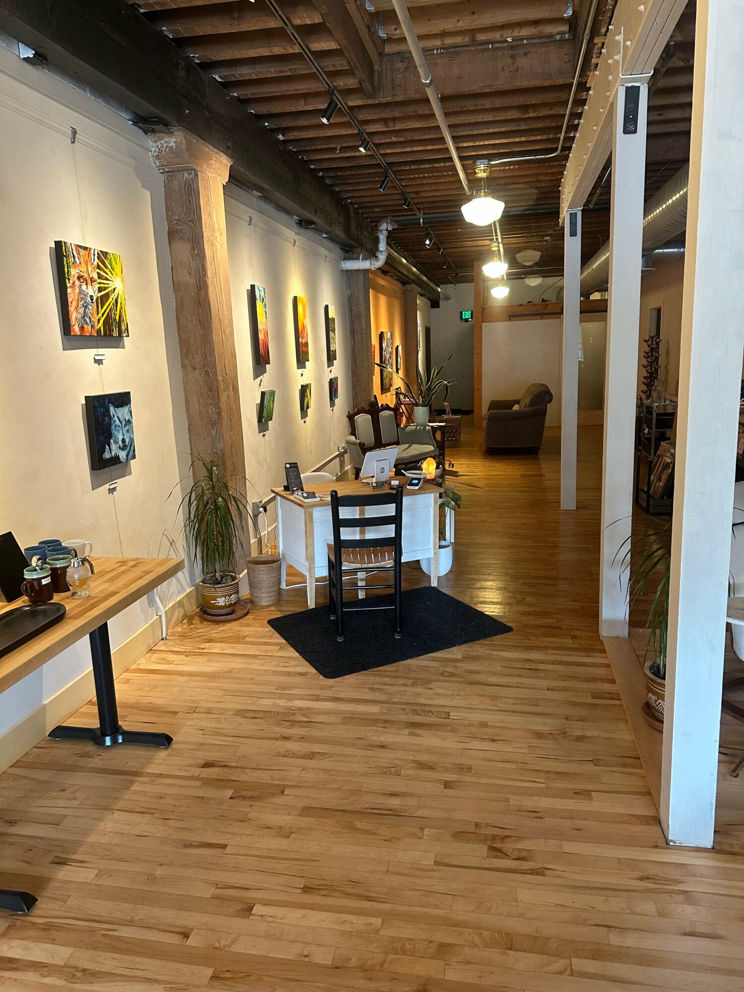 Gallery with artwork on walls, wooden floor, table set for dining, and seating area in background.