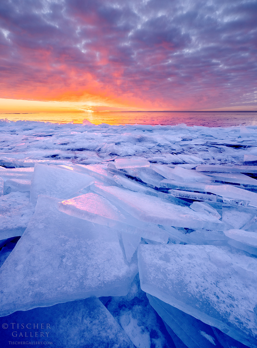 Frozen ice chunks on a body of water with a colorful sunset sky and clouds in the background.