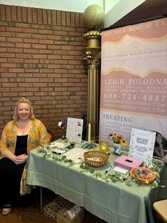 Woman sitting next to a table with various items and signs, against a brick wall and a banner background.