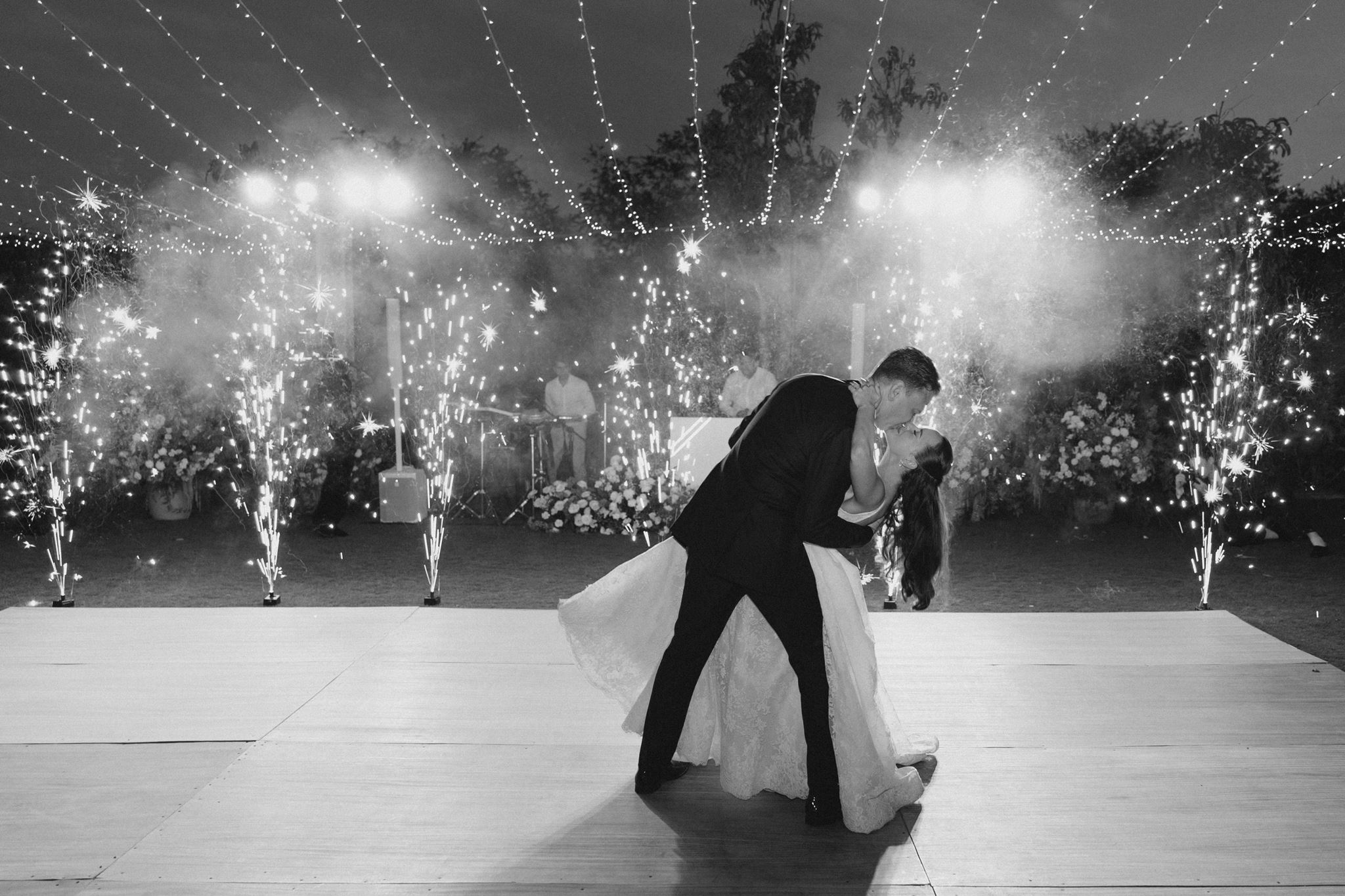 Couple dancing on a stage with fireworks and smoke in the background, celebrating at night, black and white photo.