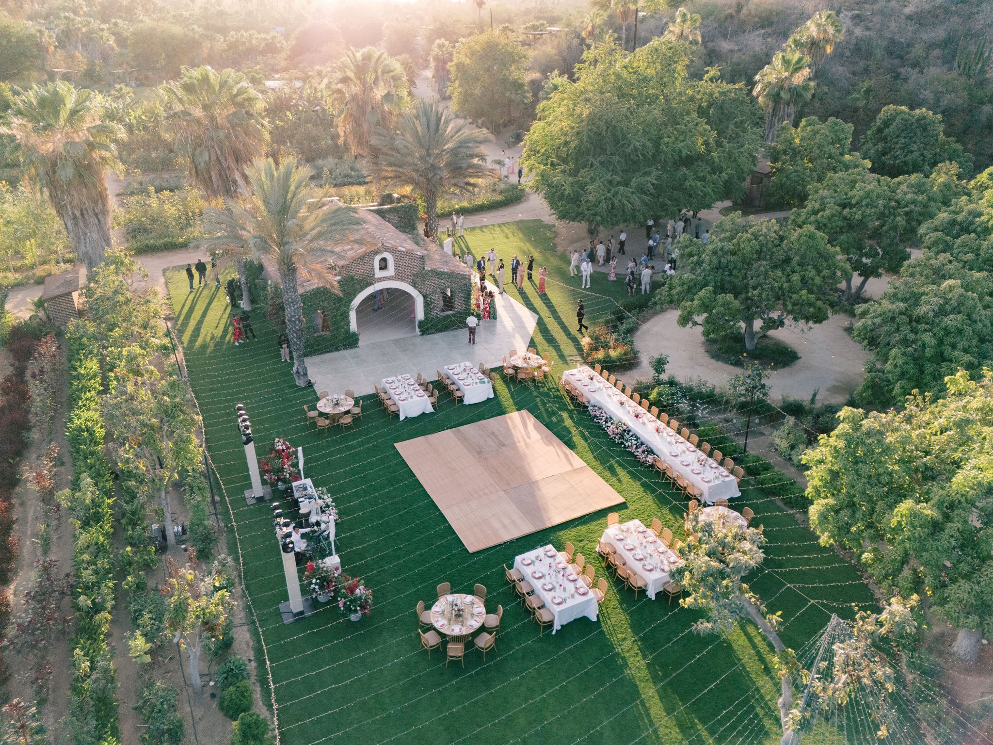 Outdoor event space with a stage, seating, and tables surrounded by trees and greenery.