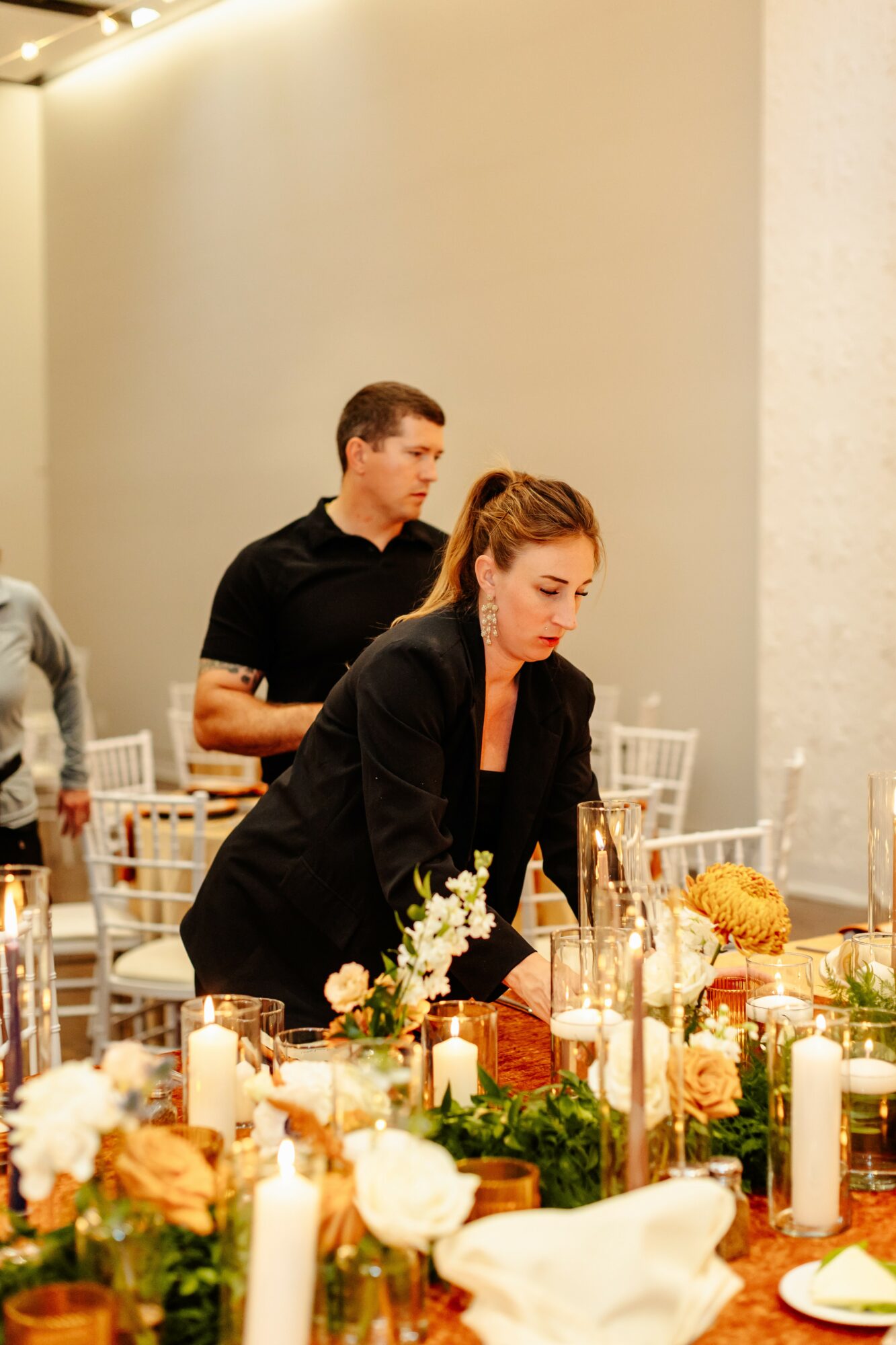 Two people arranging flowers at a table with candles and decorations, in a well-lit indoor setting.