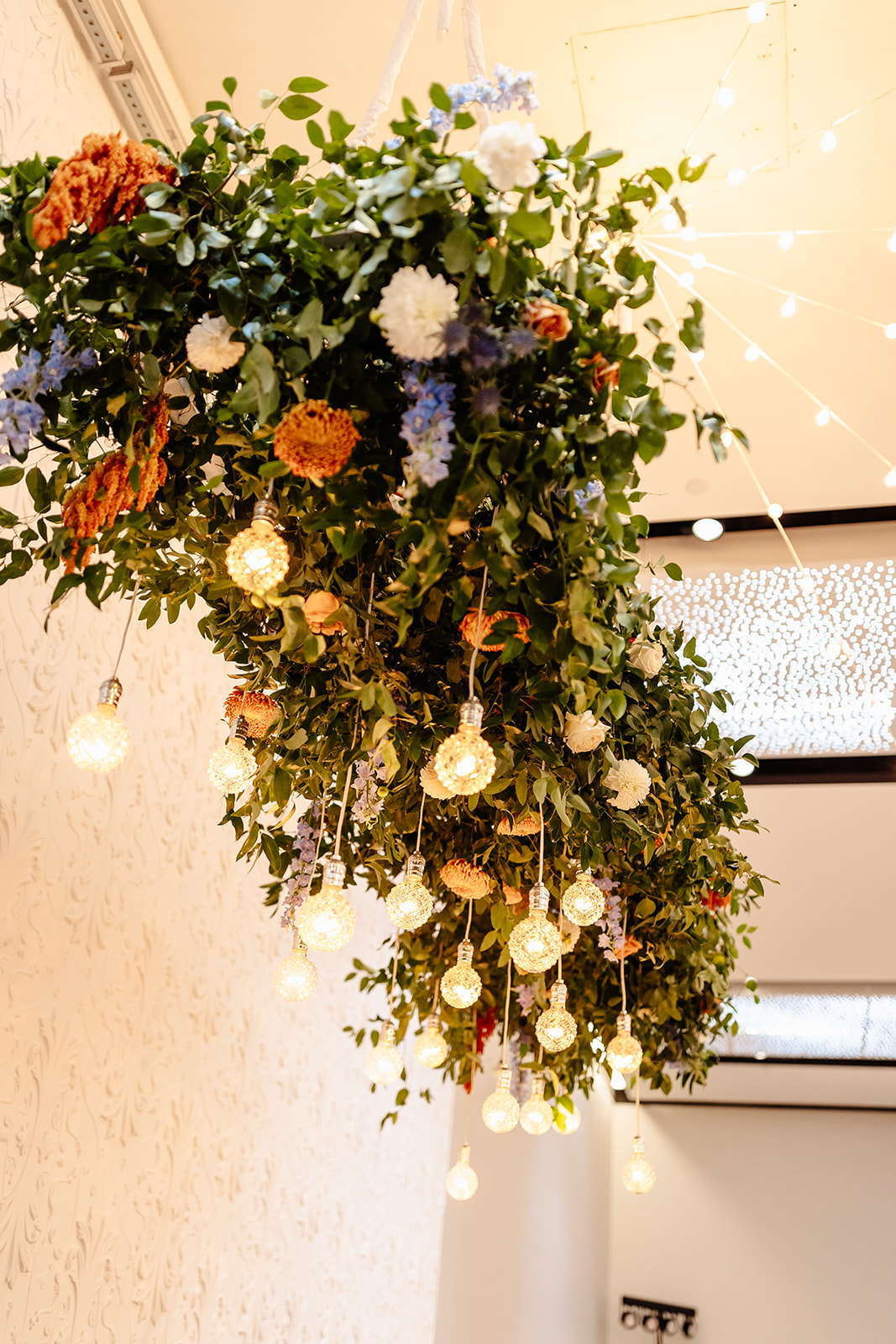 Hanging floral arrangement with lights, flowers, and greenery, cascading downward in an indoor setting.
