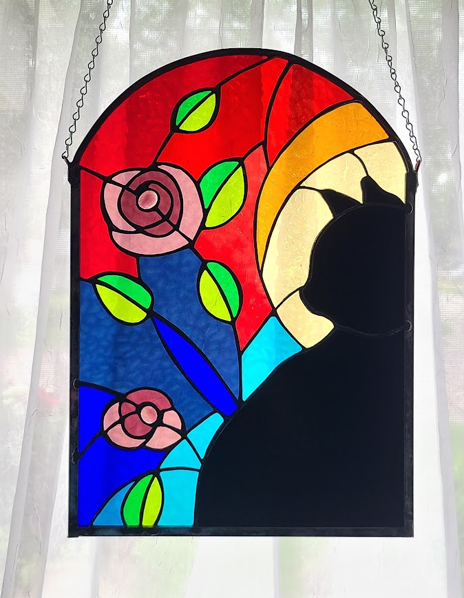 Stained glass window with a silhouette of a person, colorful flowers, and abstract shapes, hanging against a curtain background.