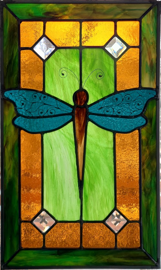 Stained glass window featuring a blue dragonfly with green and orange background elements.