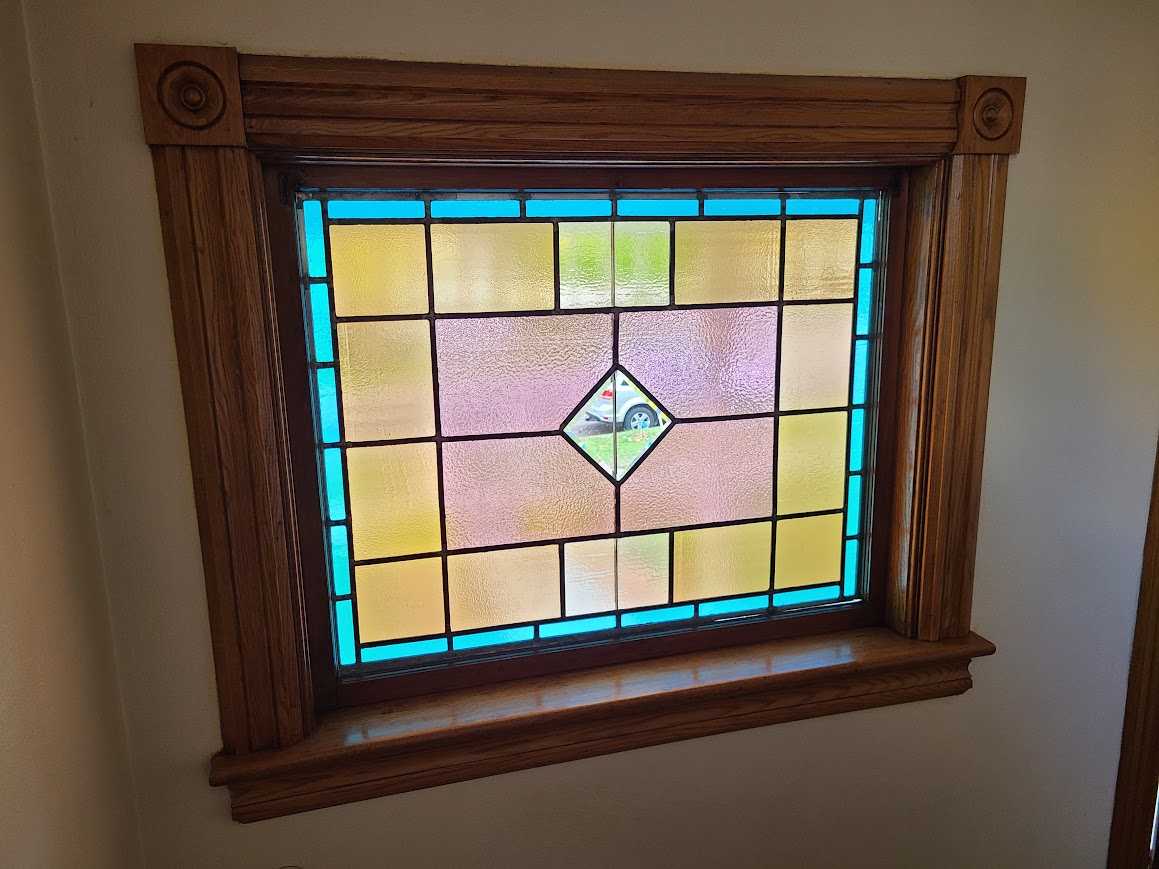Colorful stained glass window with geometric design, framed by wooden molding, in a wall interior.