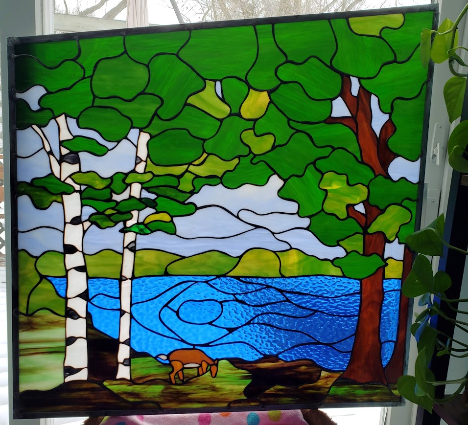 Colorful stained glass window depicting trees, a lake, and a landscape with hills, a dog, and a bird.