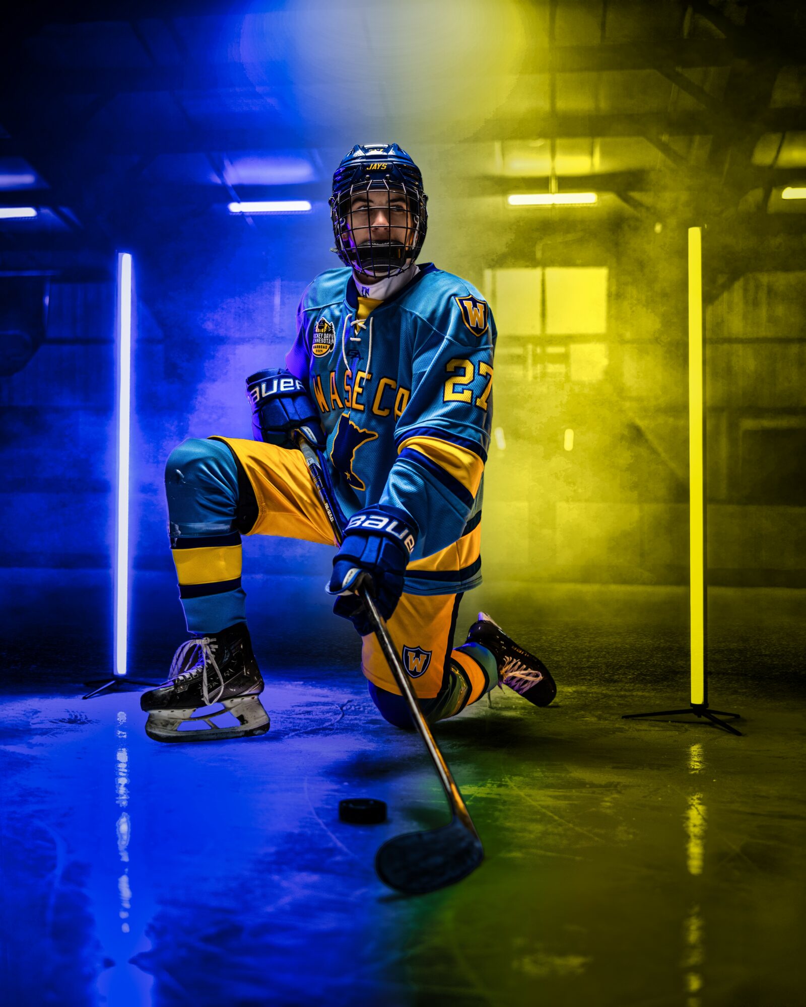 Hockey player in blue and yellow uniform kneels on ice with a stick, colorful lighting and fog effects in background.