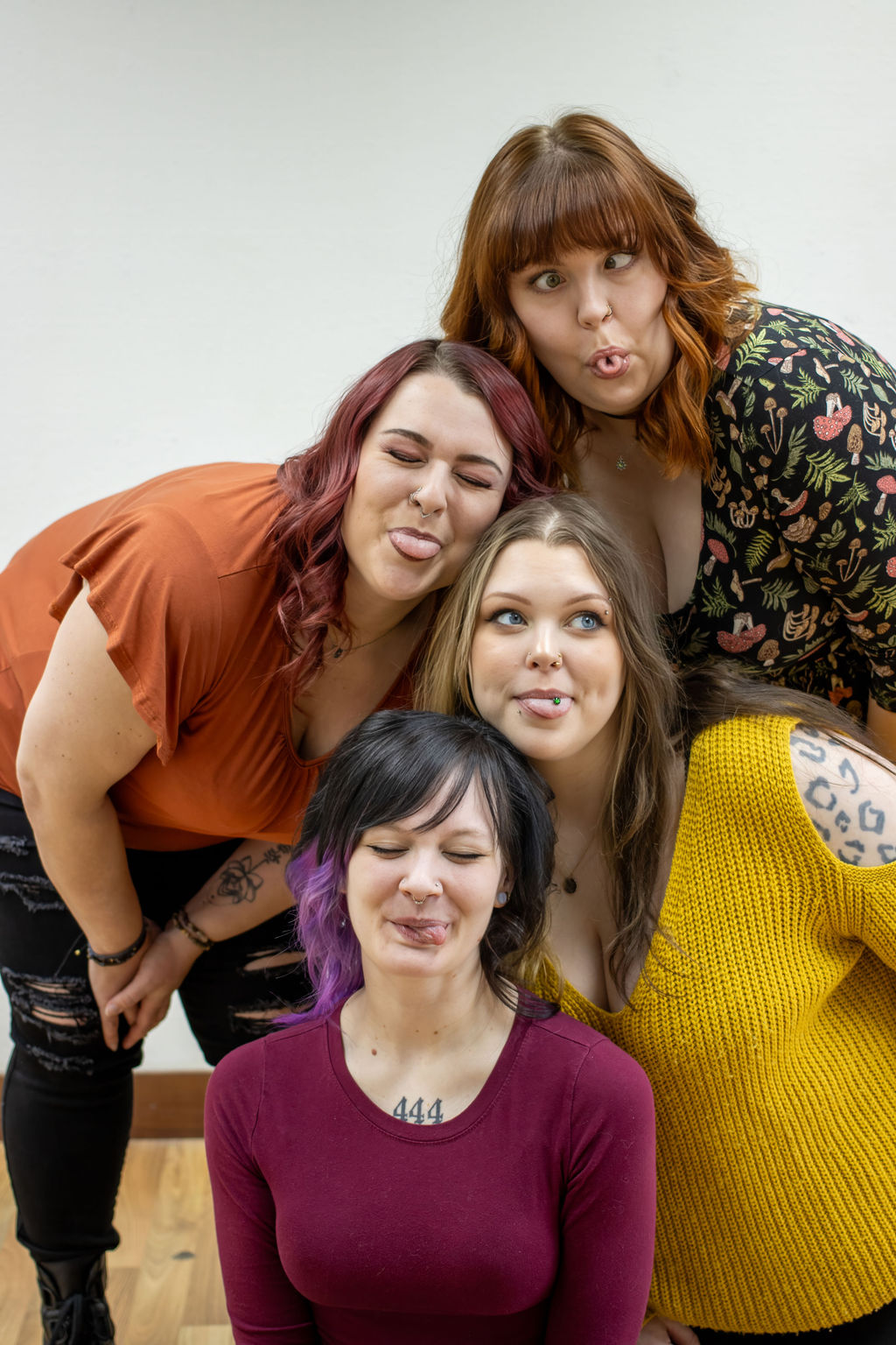 Four women posing together, making playful facial expressions, against a plain background.