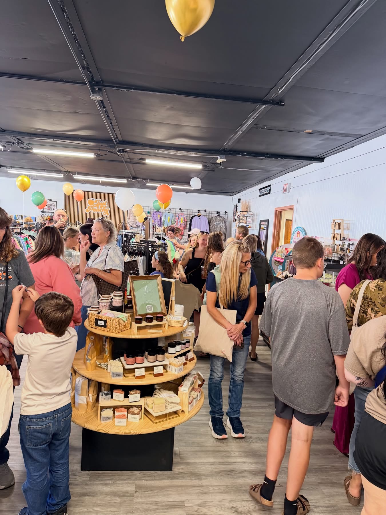 Crowd of people shopping in a store with balloons and shelves, some browsing and others talking, in a spacious indoor setting.