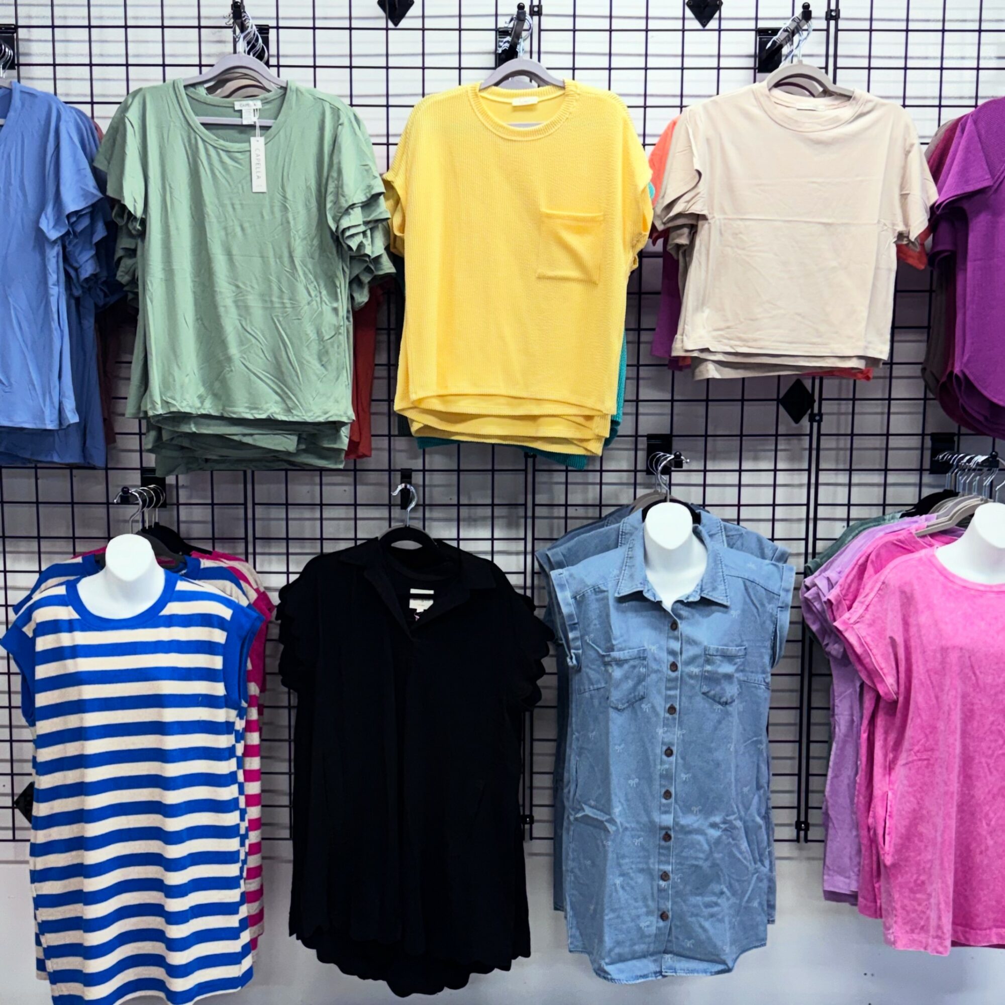 Display of colorful T-shirts and tops hanging on a grid wall, including striped, solid, and patterned styles.