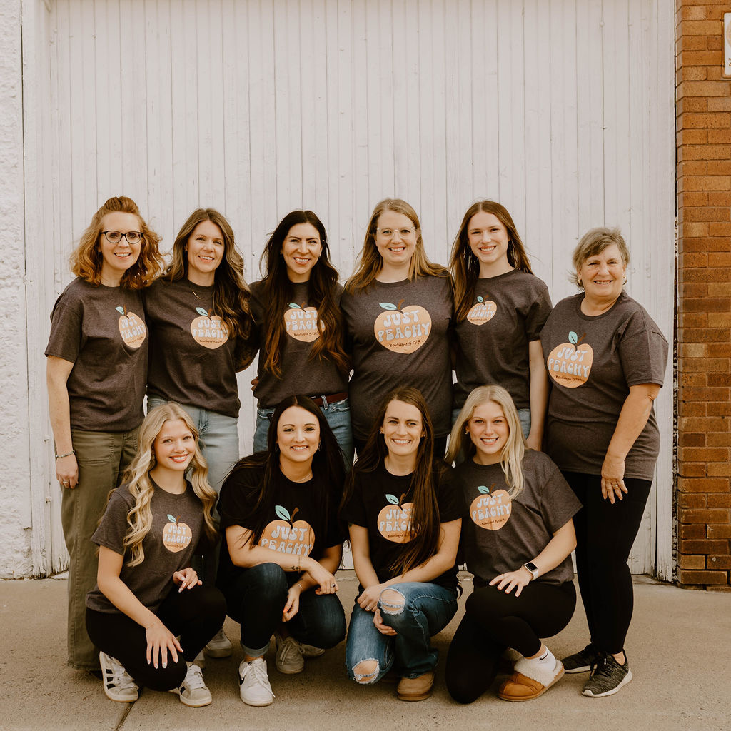 Group of ten women standing and sitting in front of a white wall, smiling, wearing matching black T-shirts with a pumpkin design.