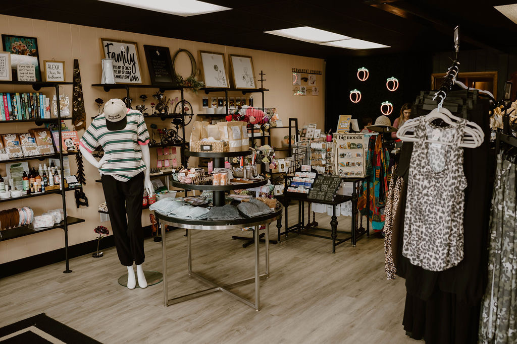 Clothing and gift items displayed on shelves and tables in a store, with a mannequin wearing a striped shirt and black pants.
