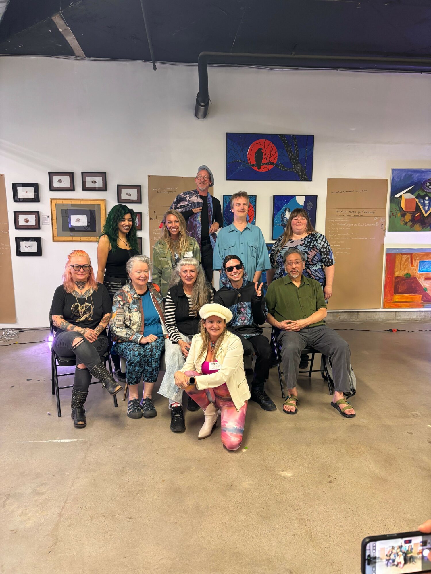 Group of people sitting and standing in an art gallery with colorful paintings on the wall.