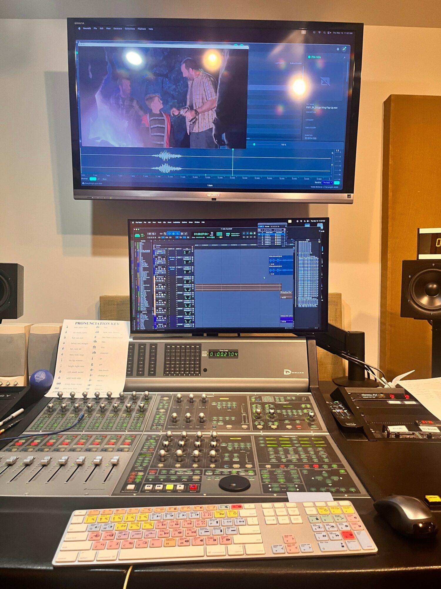 Music production studio with two monitors, mixing console, keyboard, and audio equipment on a desk.