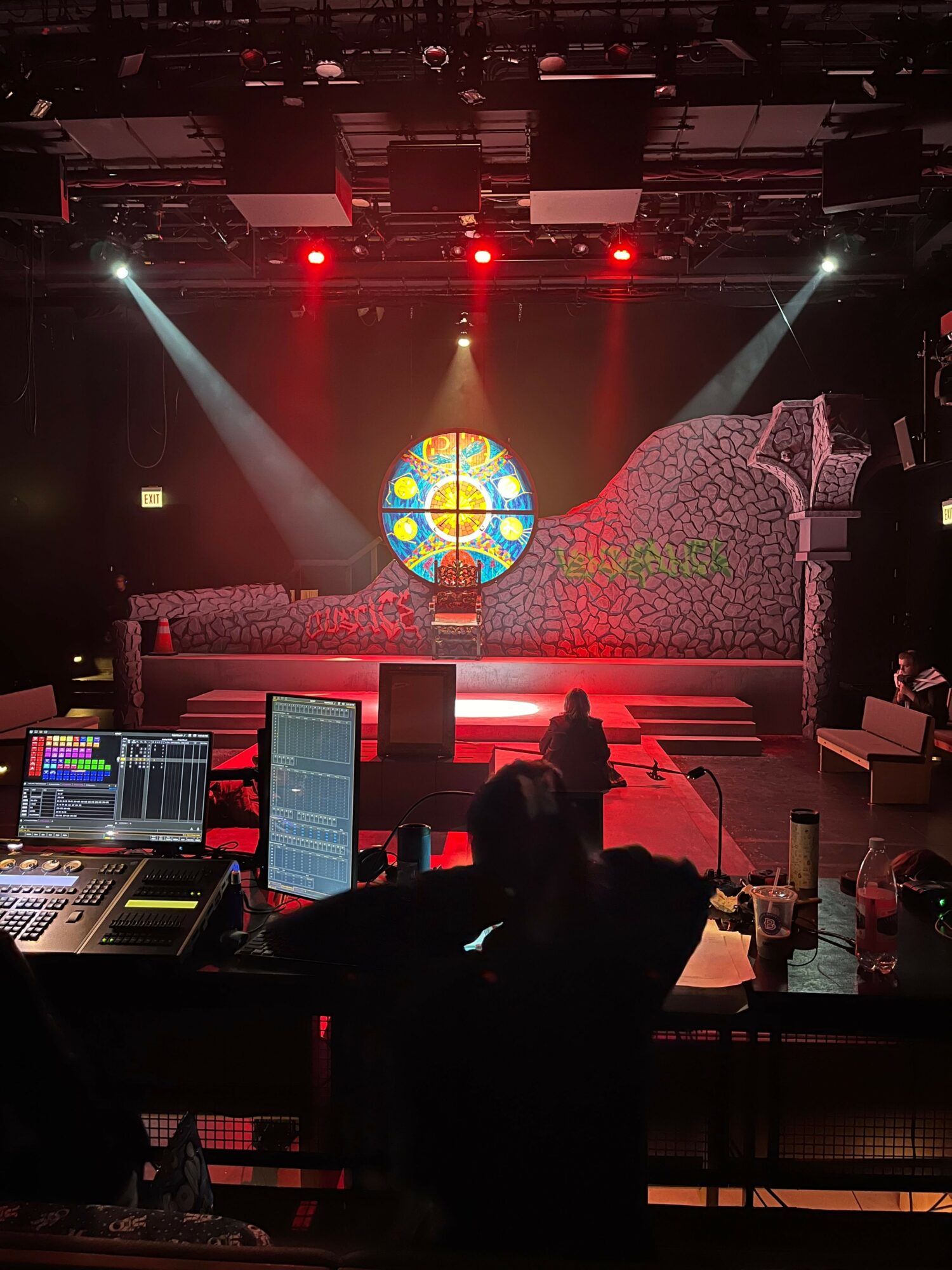 Stage with colorful circular stained glass window, bright lights, and silhouettes of people, possibly in a church or concert hall.