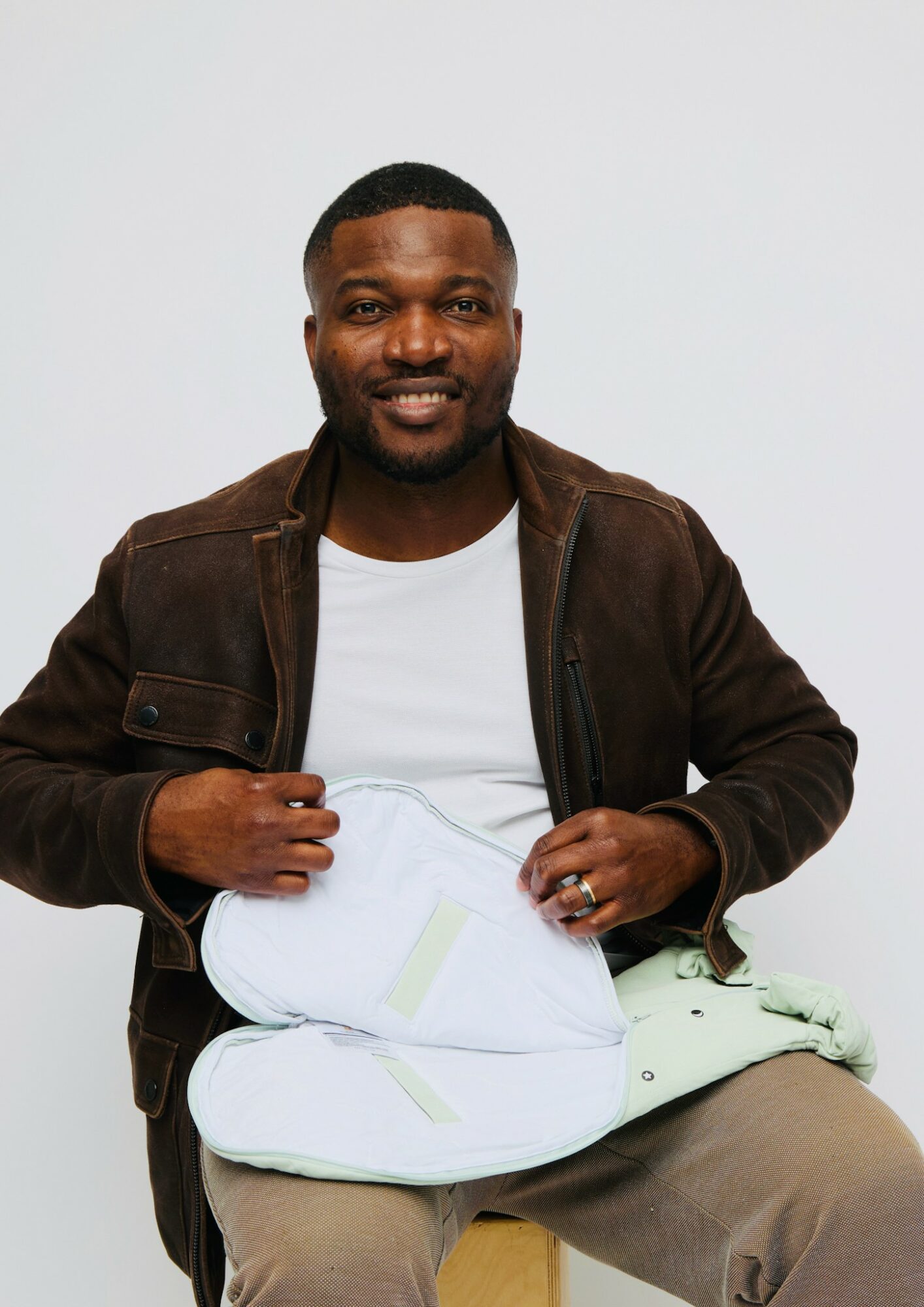 Man sitting with a baby wrapped in a blanket, smiling, against a plain background.