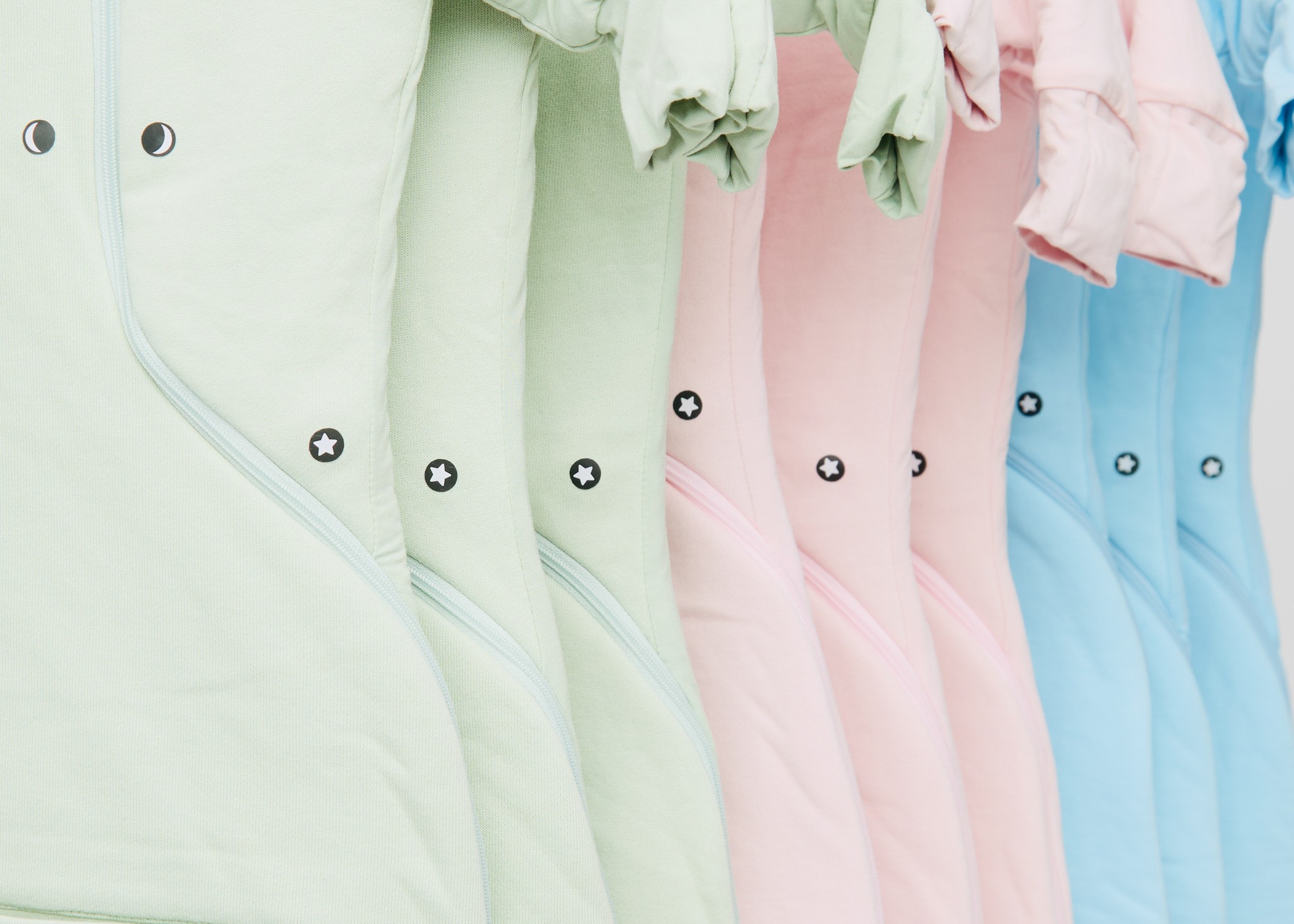 Close-up of pastel-colored baby onesies hanging, showing fabric and snap details.