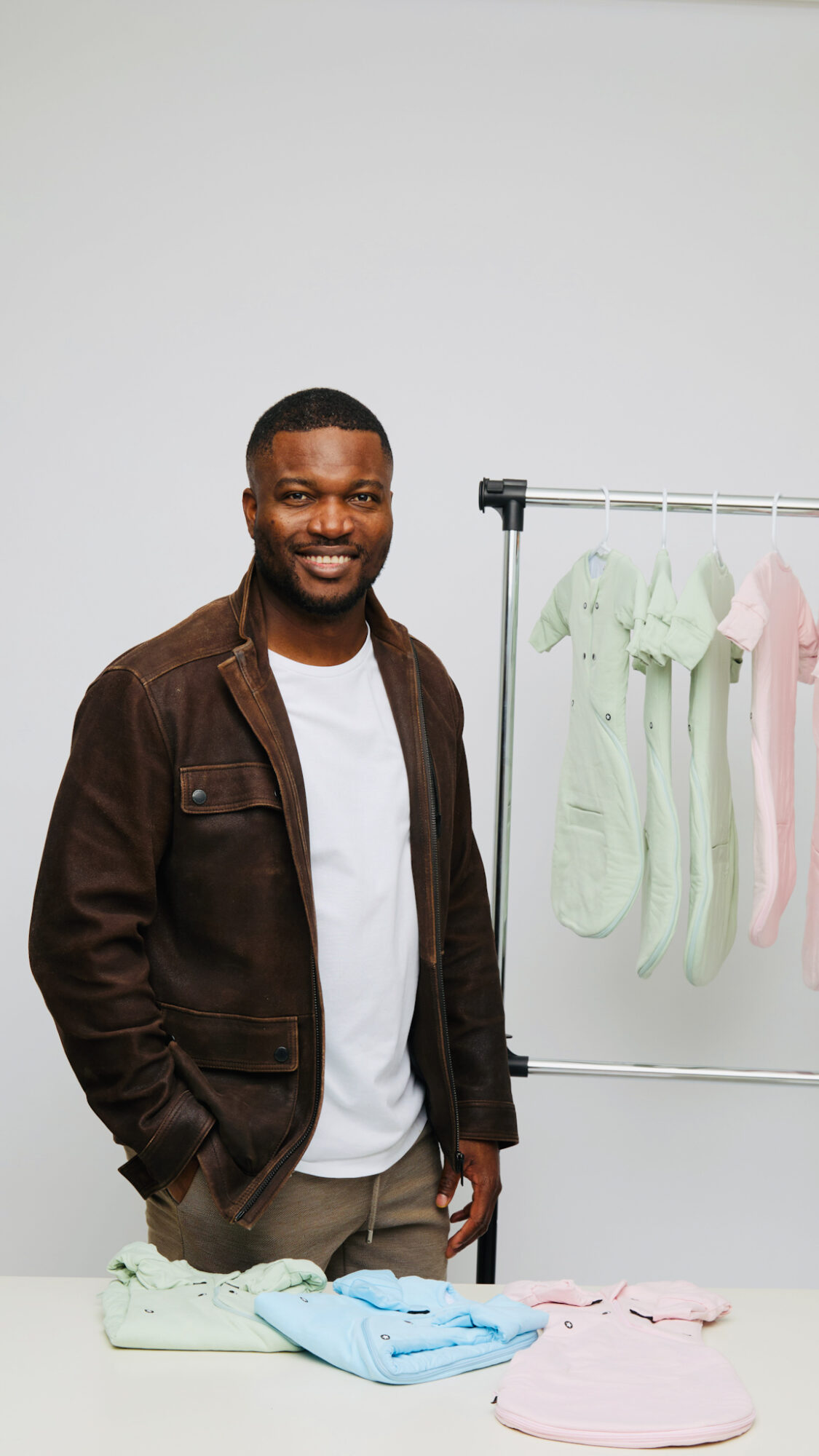 Smiling man standing next to a clothing rack with pastel-colored socks, in a plain white room.
