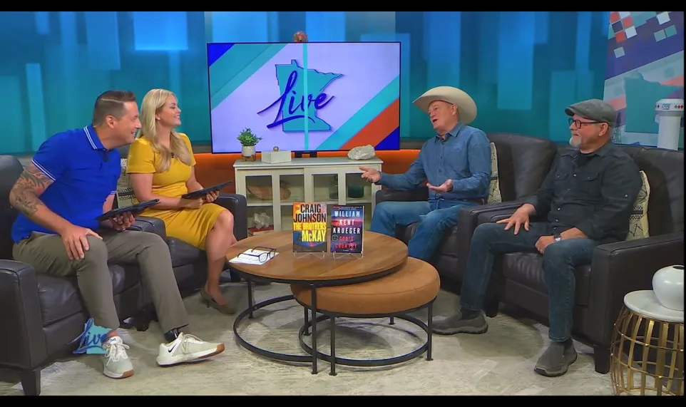 Four people sit on a TV set with a colorful background and a screen displaying the word 'live'.