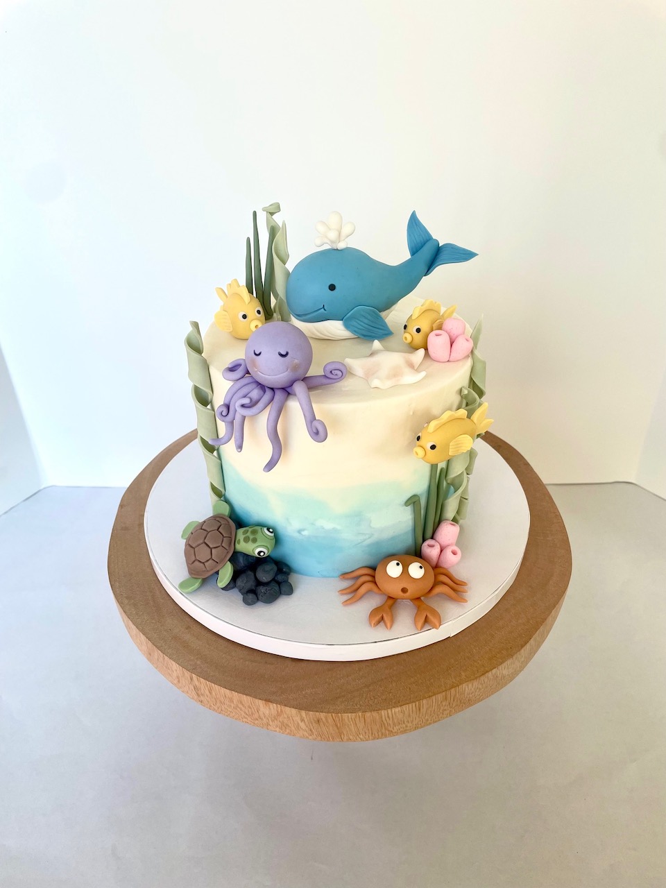Cake decorated with sea creatures including a whale, octopus, turtle, crab, and fish, on a wooden stand.